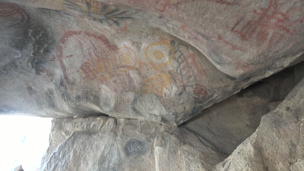 At 0:02, the upward view in Santa Rosalia shows more ceiling surface, with red pictograph lines, yellow markings, gray stone ledges, and no visible people.
