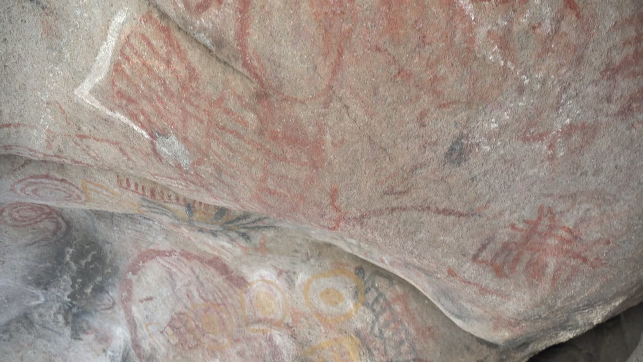 Faded red handprints, circular marks, and pale pigment traces cover a gray rock surface in Santa Rosalia, Baja California Sur, with no visible people.