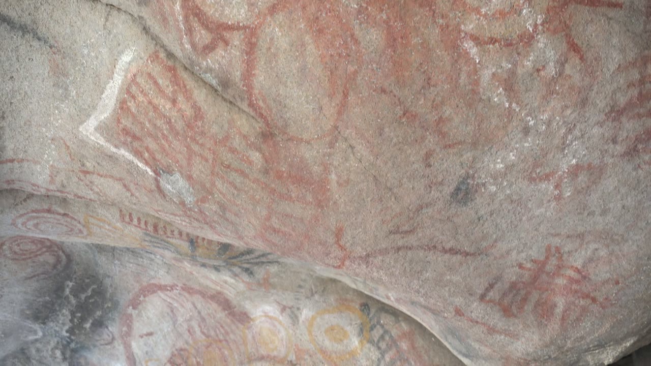 Close rock surface with red pictographs and pale streaks