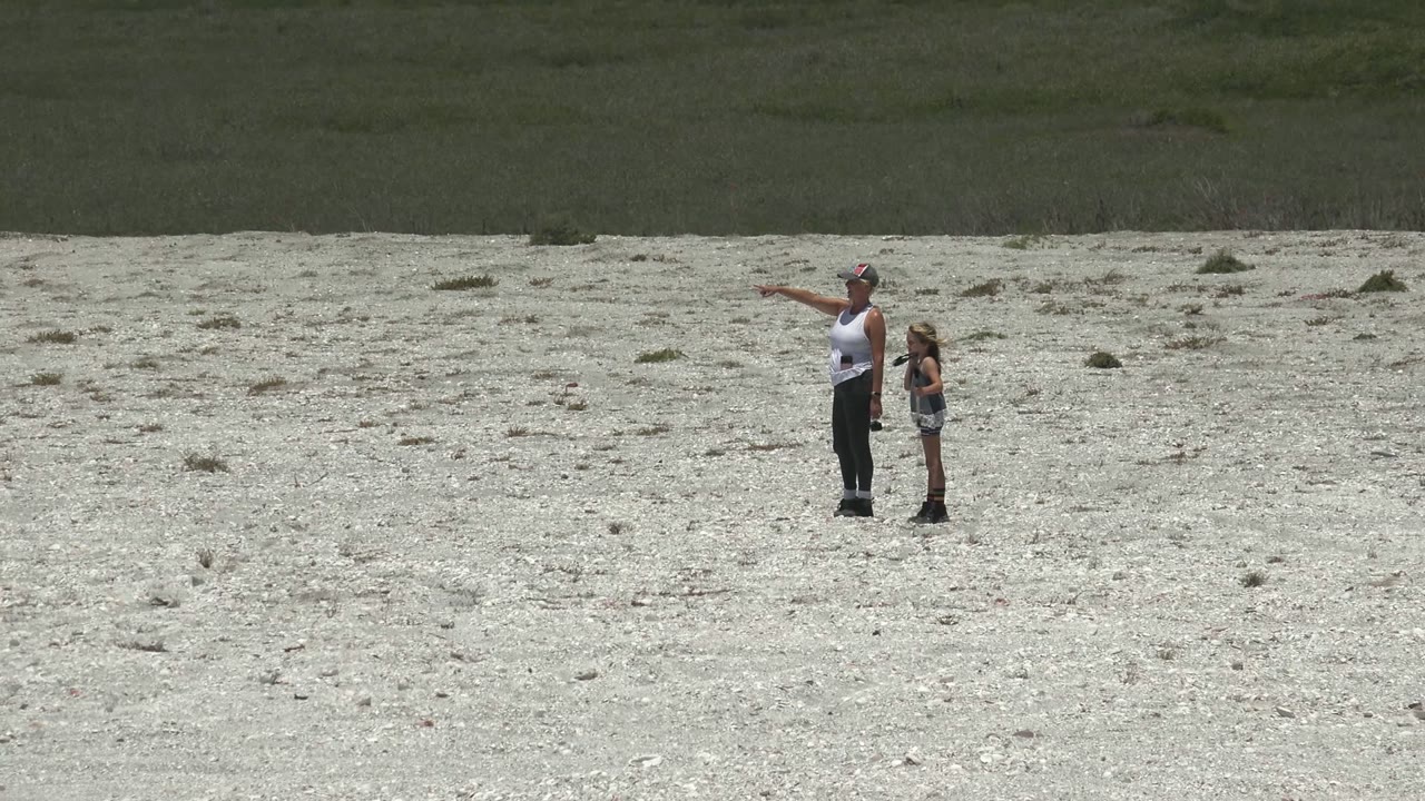 Adult gesturing beside child on rocky shoreline