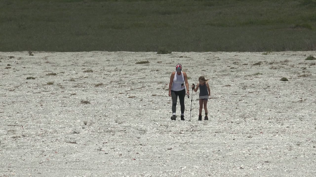 Adult and child standing on rocky ground as the child holds a stick.
