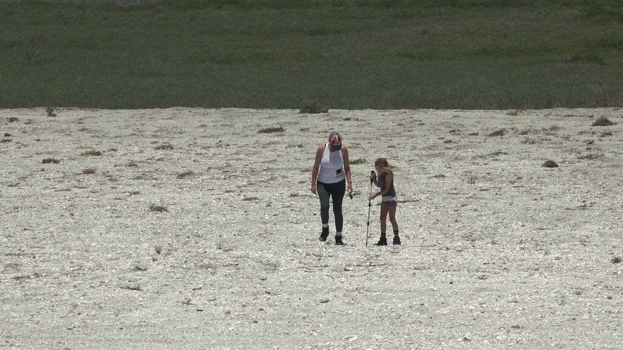 The adult stands to the left while the child stands to the right holding a stick on the pale rocky plain in San Carlos, Mexico.