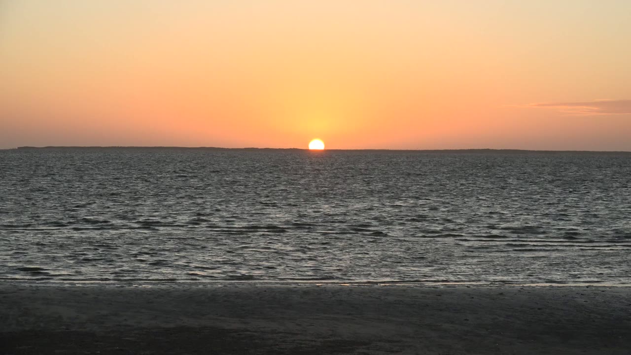 At 0:01, the sun remains low against the horizon in San Carlos, Baja California Sur, with small wave lines crossing the ocean and no visible people on the shore.
