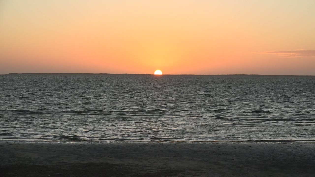 Sun touching the distant horizon over calm ocean water.