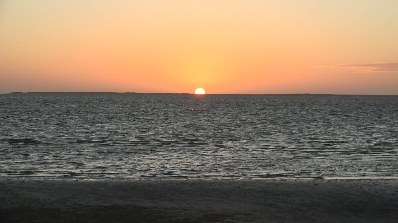 Warm orange and pink sky hangs over the ocean at San Carlos, Baja California Sur, with the sun low on the horizon and no visible people.