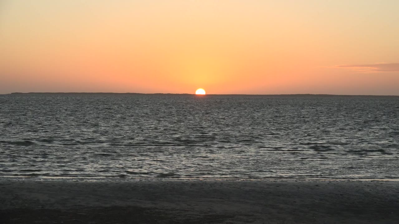 Low sunset over textured sea and empty beach.