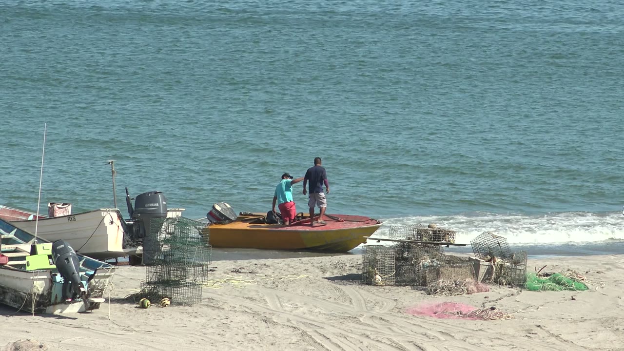 Person bending on boat while another stands near the waterline.