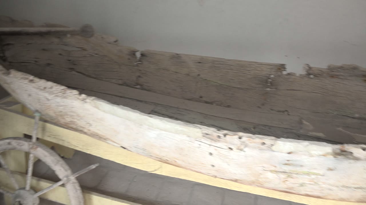Wide close view of a weathered wooden boat on an indoor stand in Mulege, Baja California Sur, with pale planks, dark worn interior wood, and no visible people.
