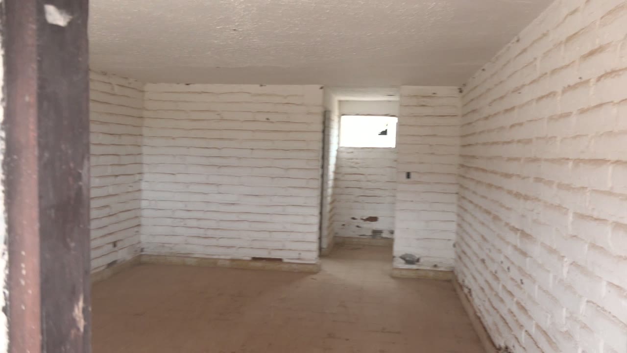 Empty white brick room with doorway edge in foreground and small window at back