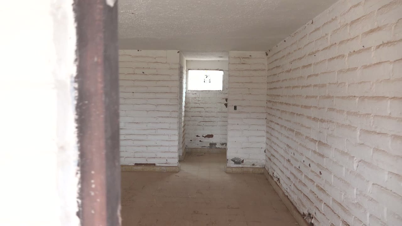 At 0:02, the view shifts along a long white brick side wall while a bright doorway post cuts the foreground and a small window remains visible at the back, with no visible people.