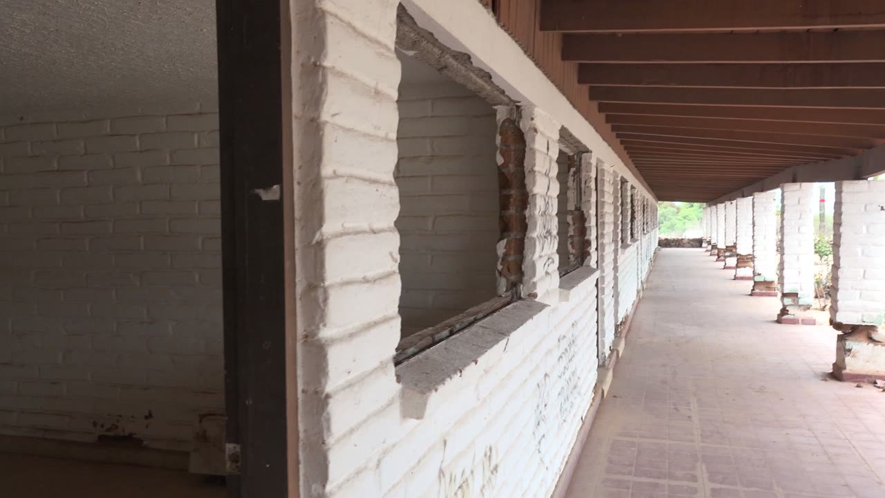 Early view down a covered white brick corridor in Mulege, Baja California Sur, with tiled floor, dark overhead beams, open sides, bright desert outside, and no visible people.