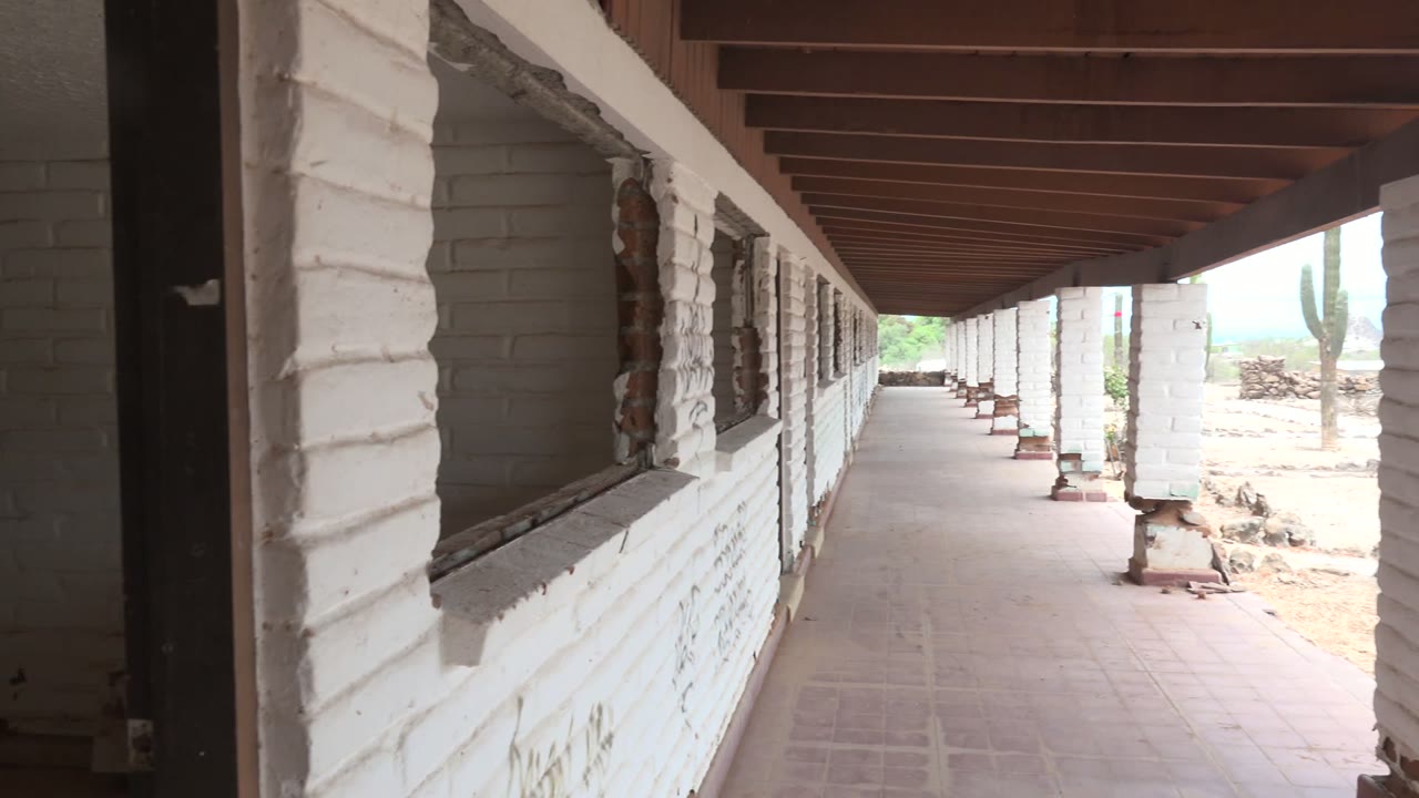 A forward view along the white brick colonnade shows the tiled walkway under dark beams, with cactus and dry terrain appearing through the open side in Mulege, no visible people.