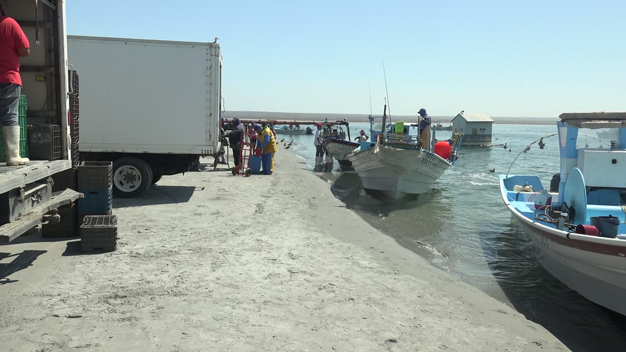 At La Bocana, the foreground boat sits closer to the right edge as people stand between the white truck and small boats at the shoreline.