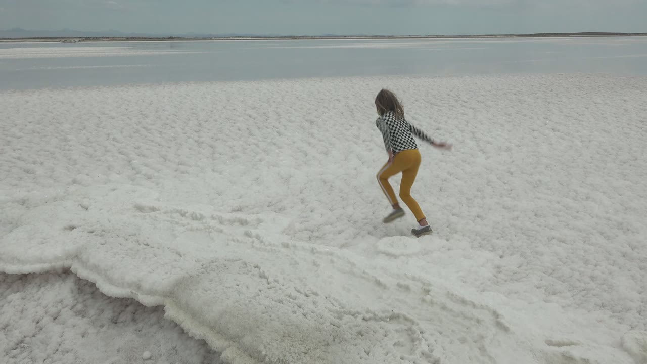 The person begins to stand on the white salt flat in Guerrero Negro, Mexico, with one arm extended and the waterline stretching across the background.