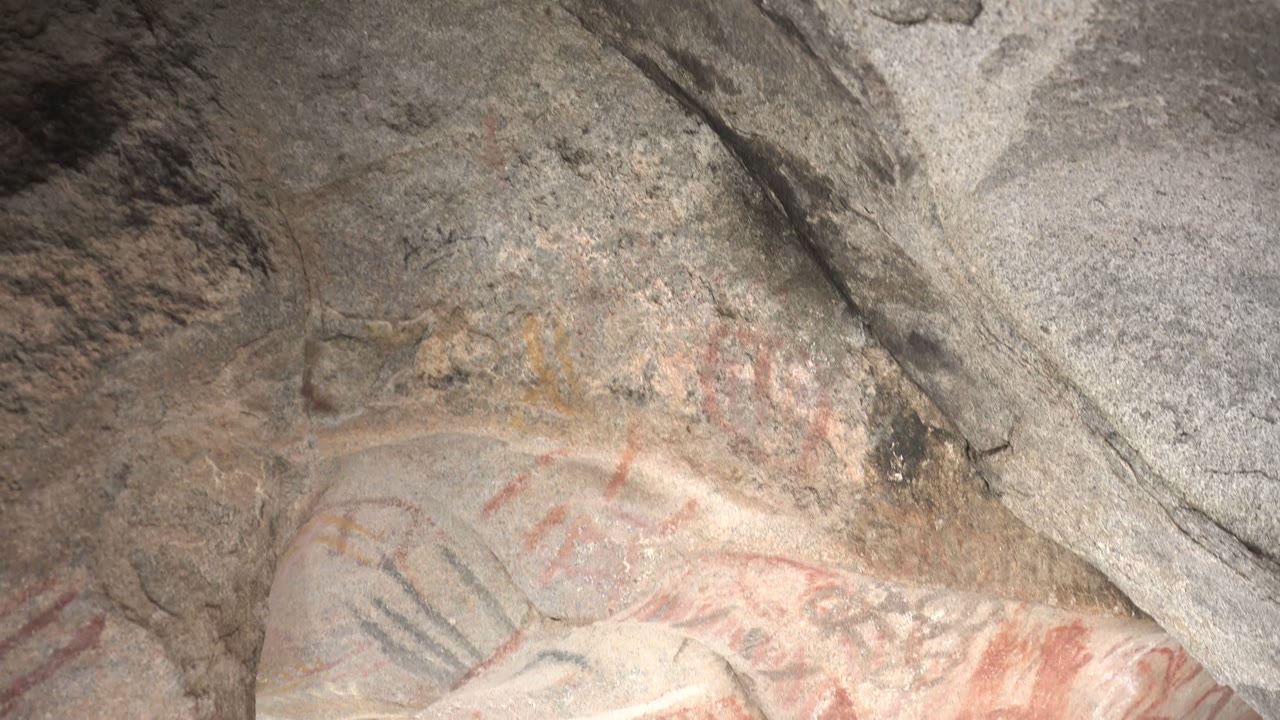 Red hand-like markings and dark lines on rough cave rock.