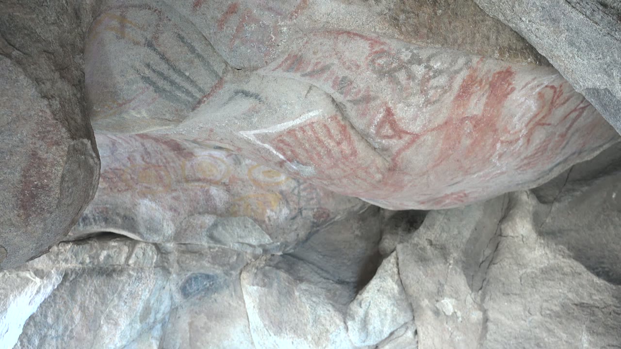 Third frame of ancient red pictographs and dark marks on pale gray stone in Santa Rosalia, Baja California Sur, with the painted ceiling filling the view and no visible people.