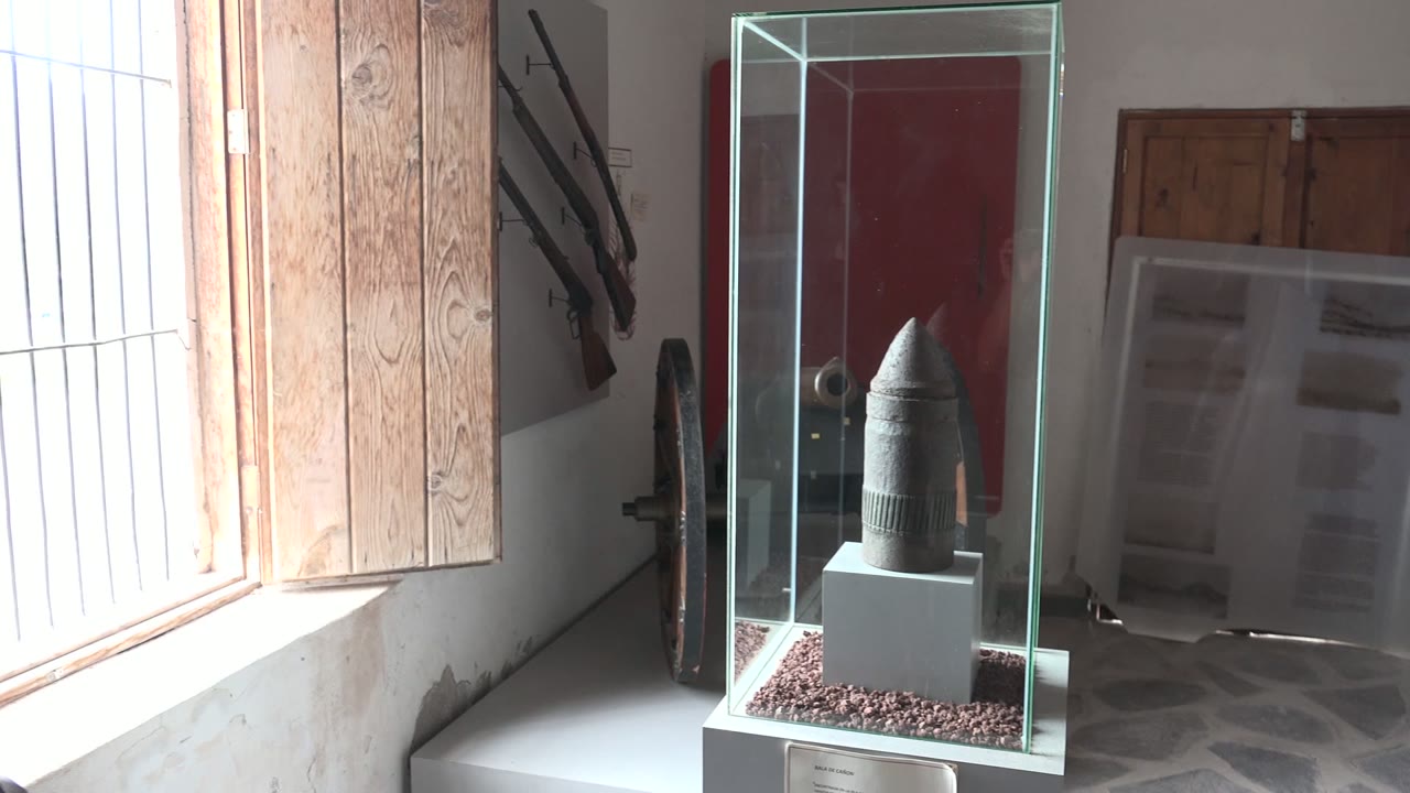 Glass museum case with artifact, red door, and barred window in background.