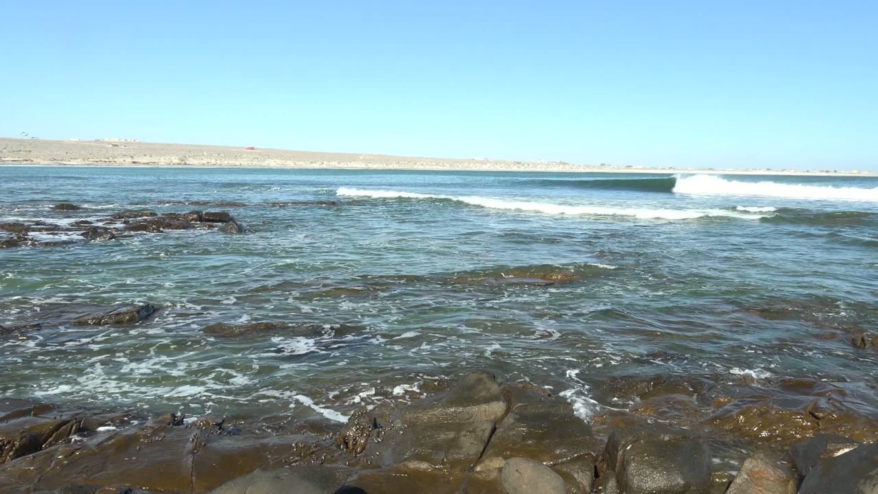 Foamy surf over rocks with a clear horizon and blue sky.