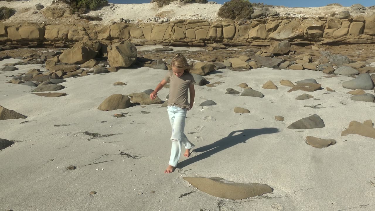 Child stepping across pale sand between beach rocks.