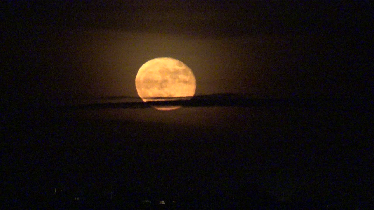 Orange full moon above a dark mountain silhouette in a black sky