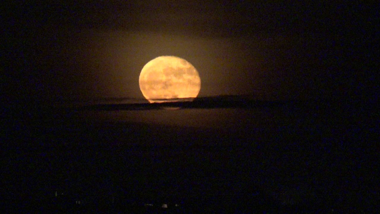 Orange moon slightly higher above the black horizon.