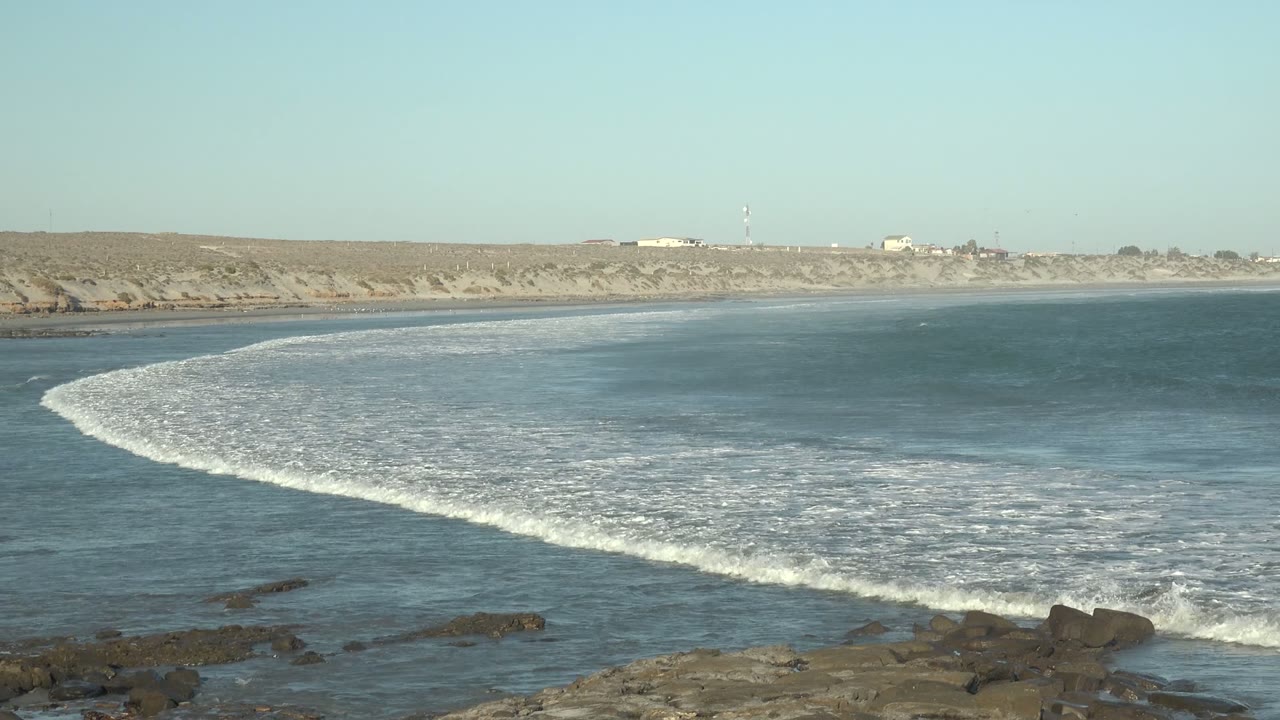 Gentle surf rolls in beside rocks under a clear sky.