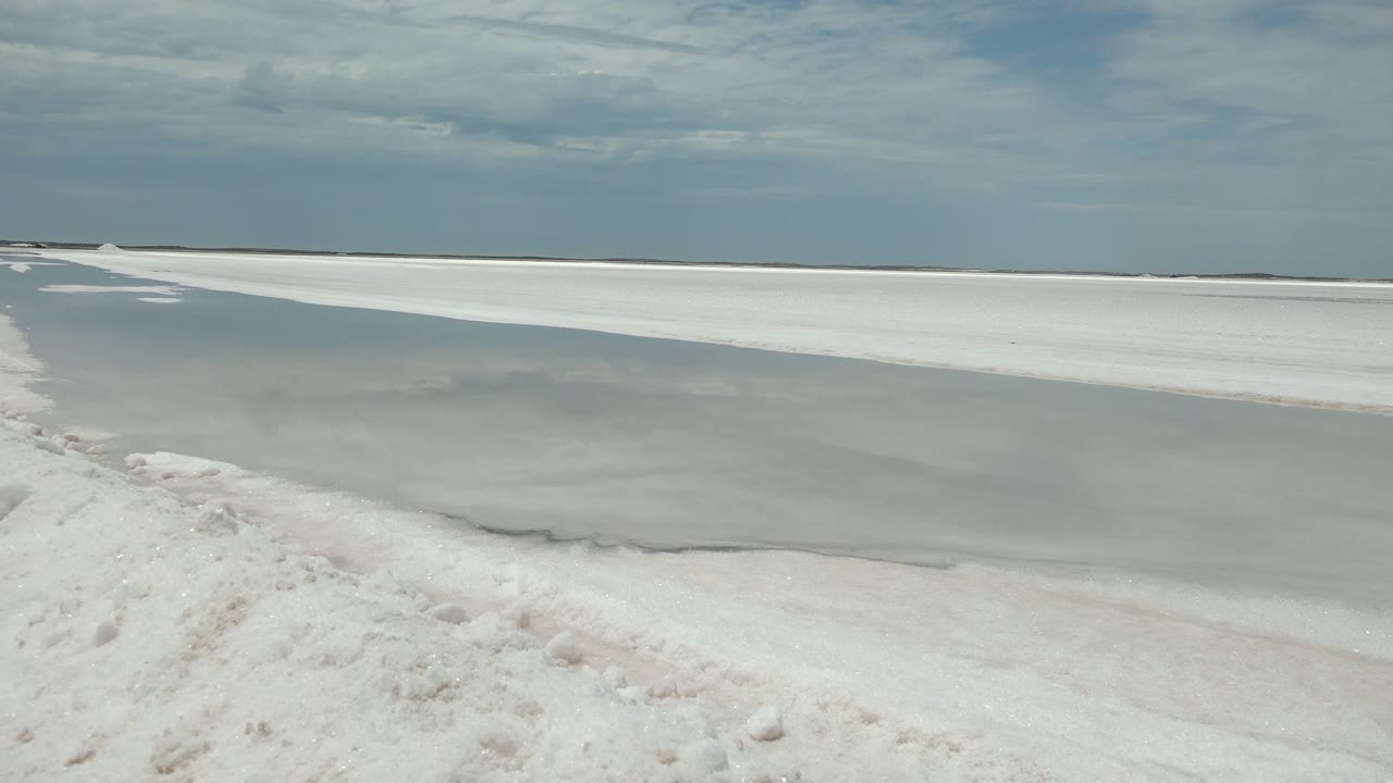 The white ridge along the shore sits close to frame as pale water stretches toward a flat horizon in Guerrero Negro, Baja California Sur, with no visible people.