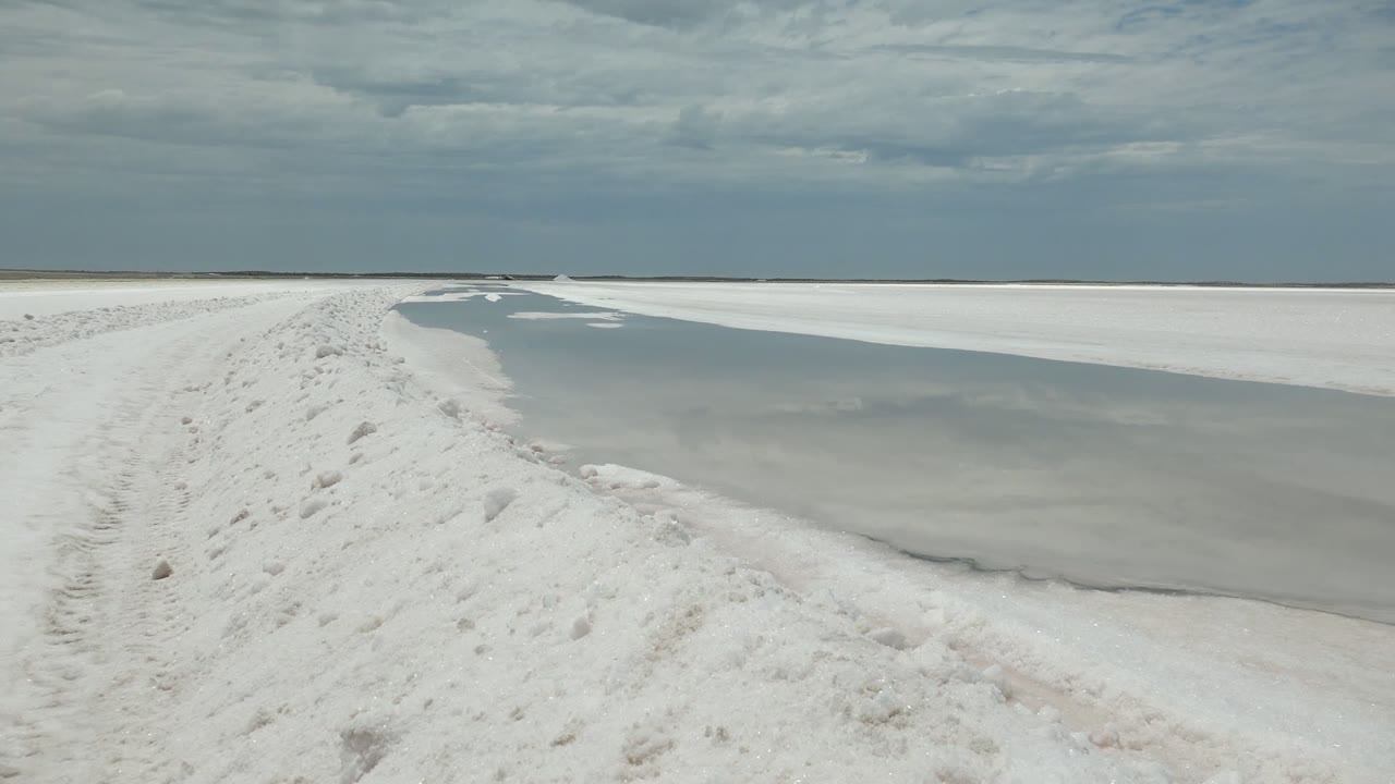 Guerrero Negro, Baja California Sur frame showing a white path curving beside gray frozen water under heavy clouds, with no visible people.
