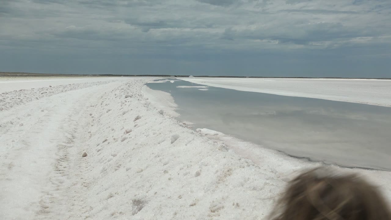 Guerrero Negro, Baja California Sur frame showing the frozen water, white path, dark cloud band, and the top of a person's head entering at the lower right edge.