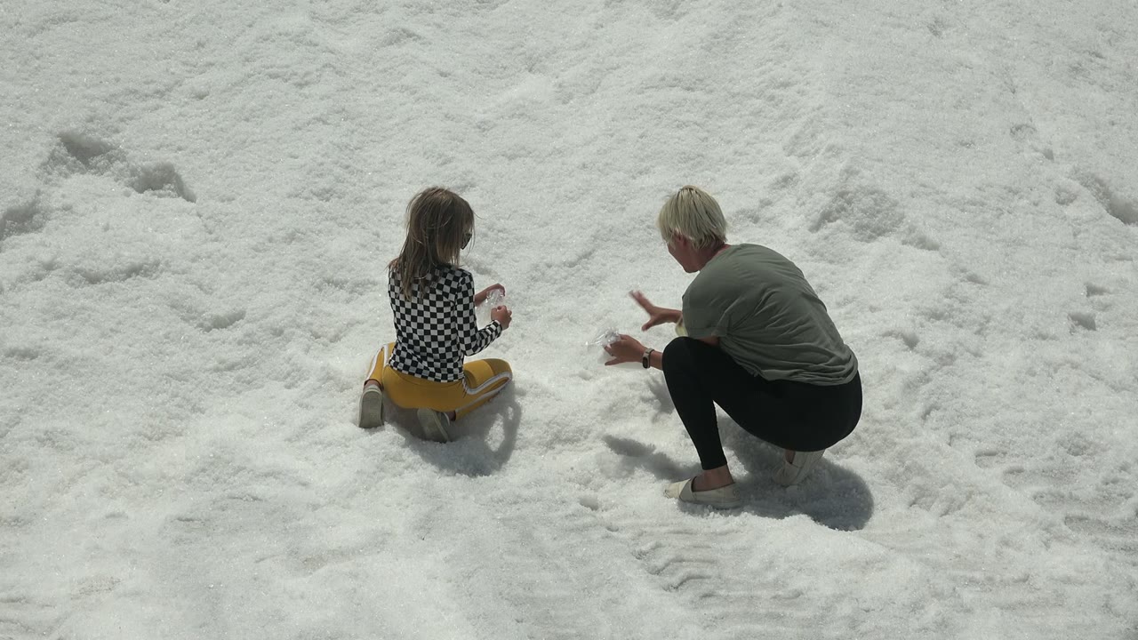 At 0:00 in Guerrero Negro, Mexico, a child sits on the white snow facing an adult who crouches with hands raised nearby.