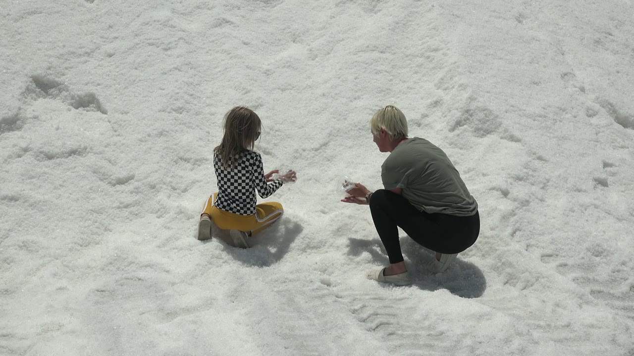 Child and crouching adult facing each other on snow.