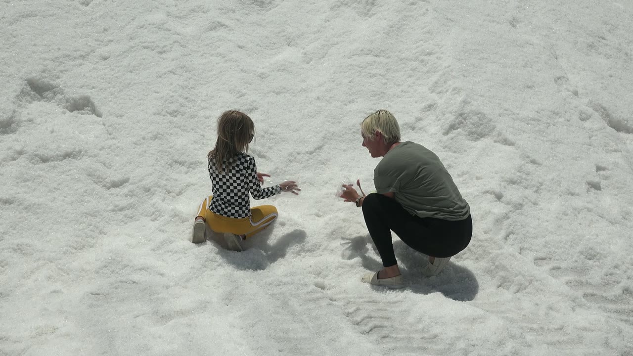 At 0:02 in Guerrero Negro, Mexico, the adult's hands are lifted near the snow while the child sits slightly turned toward them.