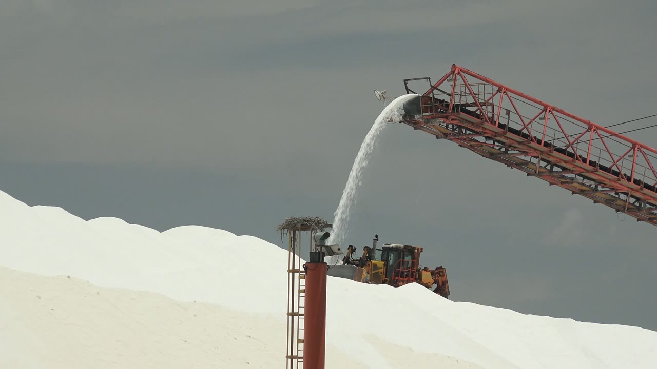At 0:02 in Guerrero Negro, Baja California Sur, the conveyor spans diagonally above the bright mound as the deposited material lands near the pile crest, with no visible people.