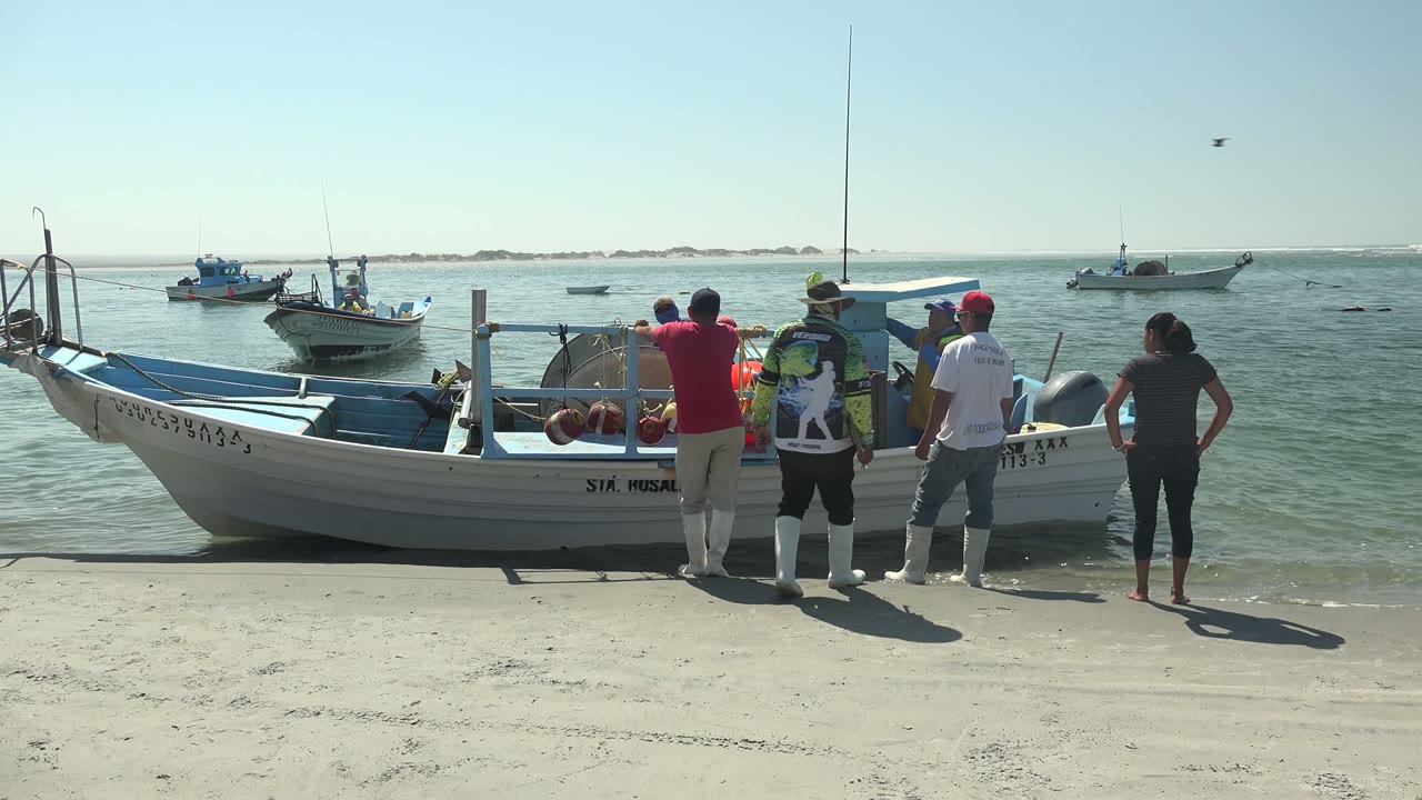 Group at the side of a beach boat with crates and offshore boats in the background.