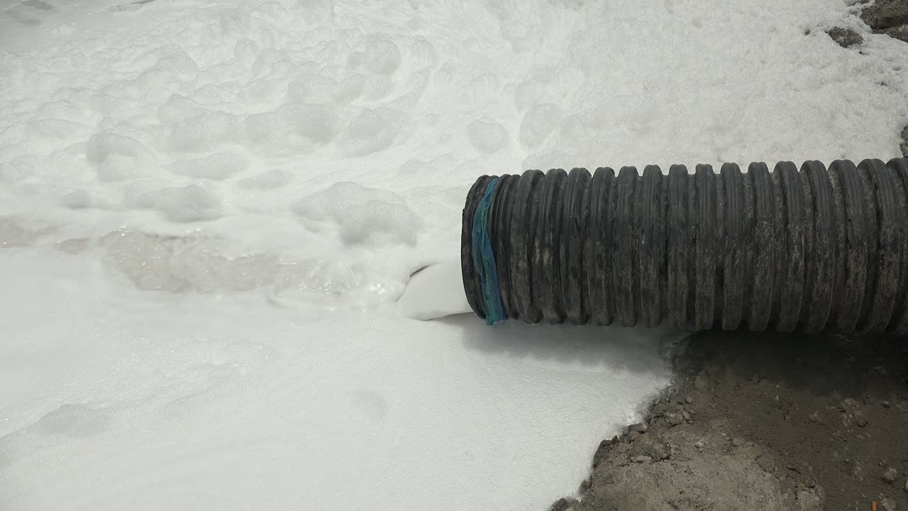 Ribbed hose lying over white foam with wet ground below