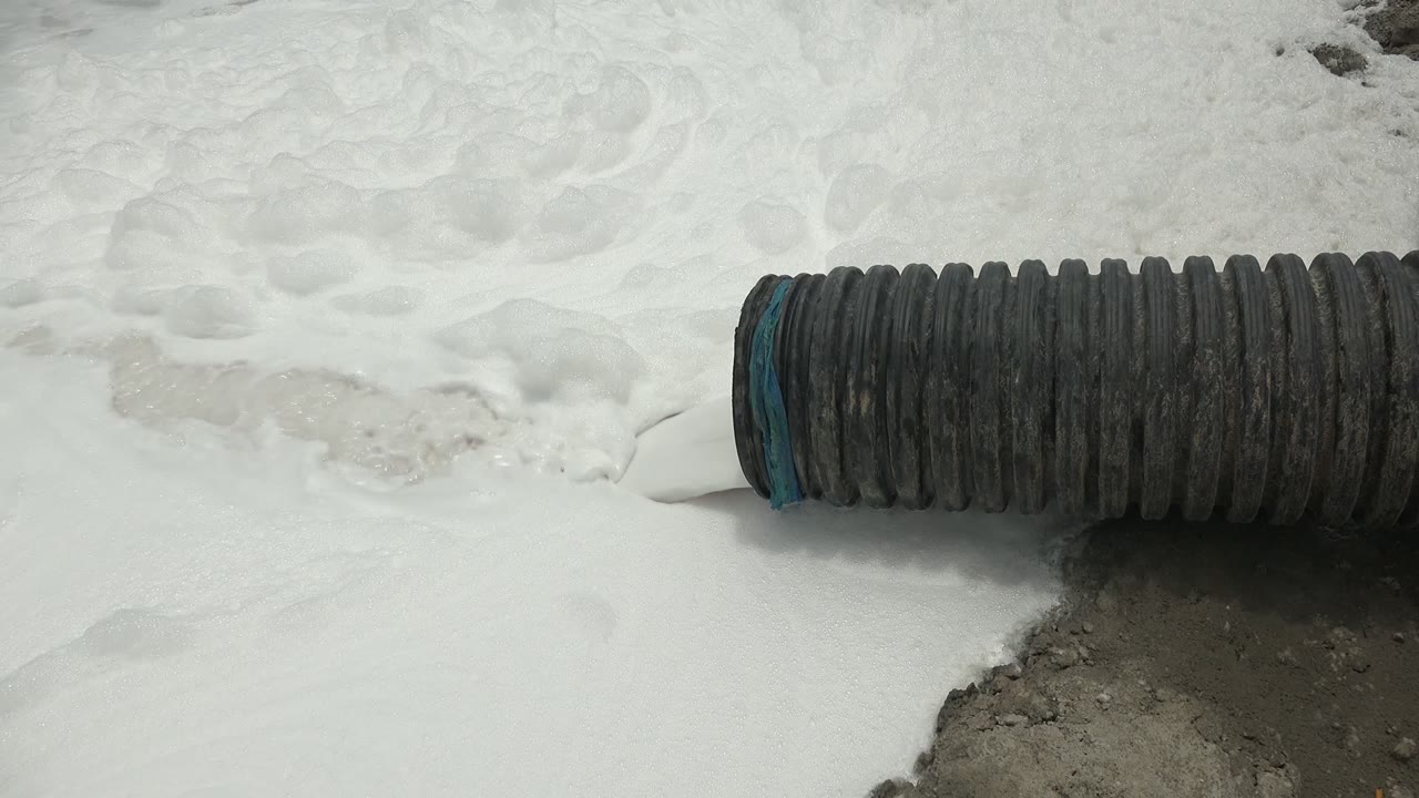 At 0:02 in Guerrero Negro, the corrugated hose stretches across the frame with white foam gathered around the left opening and no visible people.