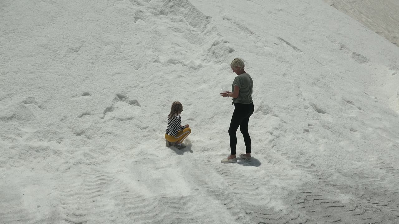 Adult standing beside seated child on bright sand.