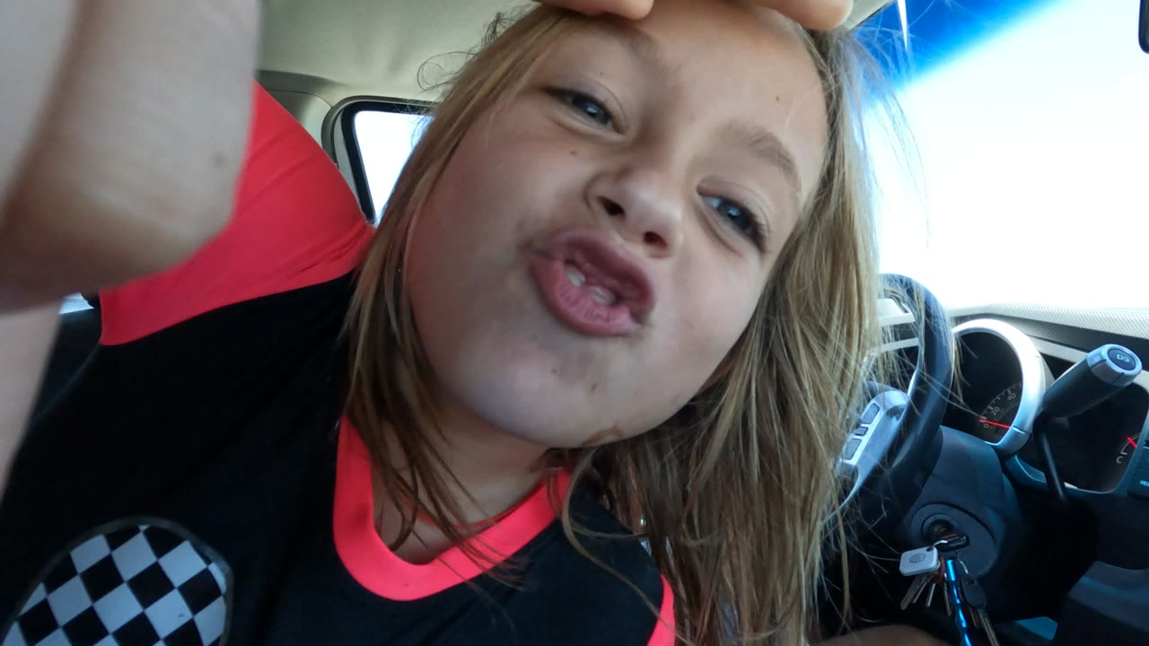 Child puckering lips near the camera in a car interior.