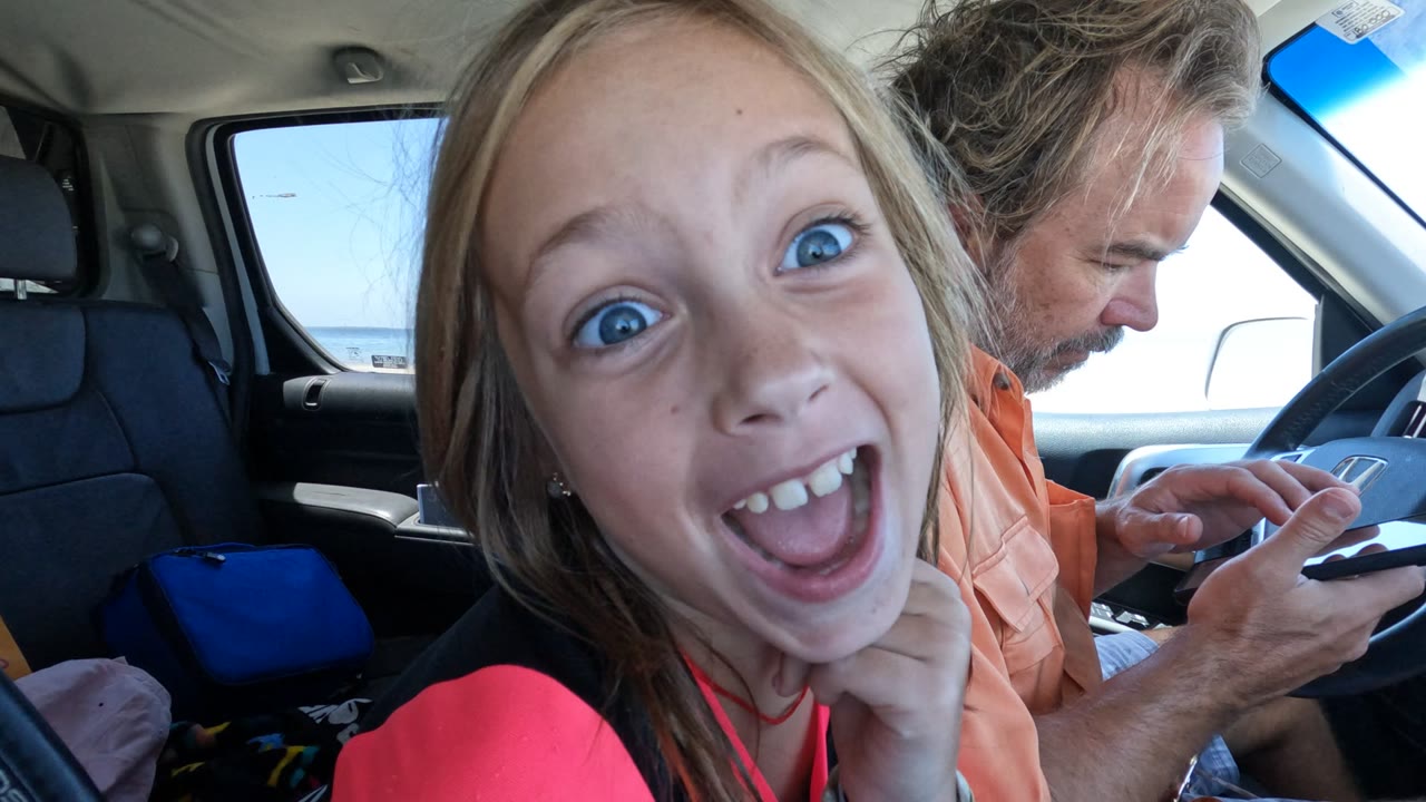At 0:02 in Baja California, Mexico, the girl opens her eyes wide and grins close to the lens while the driver remains partly behind her with a phone in hand.