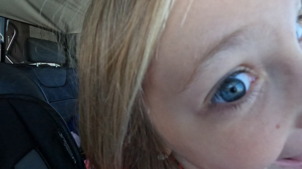 Extreme close-up of a girl's blue eyes and face inside a car.