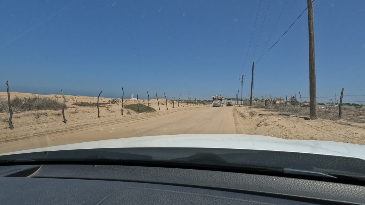 At 0:00, a windshield view in Baja California, Mexico shows a sandy road, fence posts, utility poles, dry scrub, an oncoming vehicle in the distance, and no visible people.