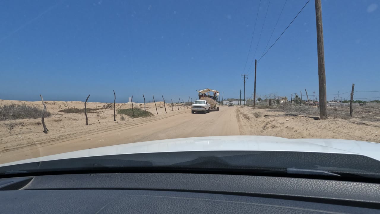 White pickup truck farther along a sandy road seen over a car hood.
