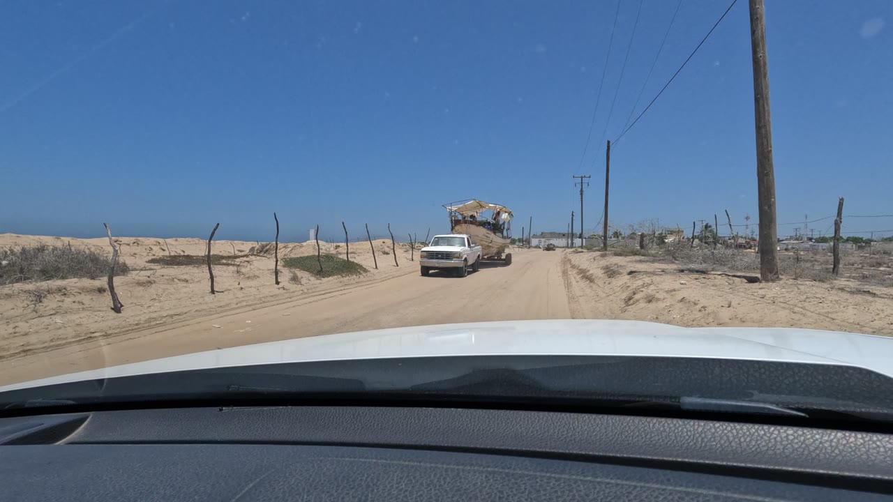 White pickup nearing the car on a sandy road with utility poles.