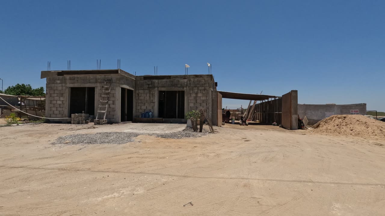 Cinder block building with open doorways, gravel, sand piles, and utility poles.