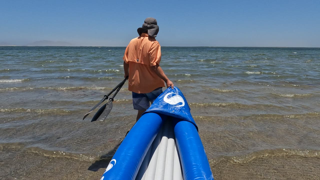 At 0:02 in Baja California, Mexico, the bright blue boat fills the lower frame while the person holds the paddles near the rippled shoreline.