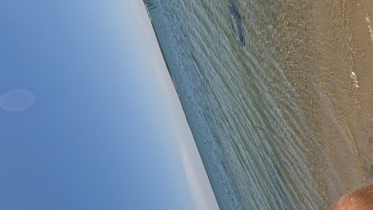Tilted Baja California beach view with clear shallow water over sand, blue sky at left, and no visible people.
