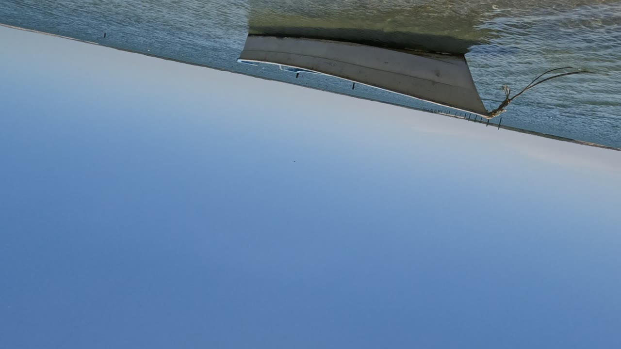 The tilted camera angle continues over Baja California water, with a hard shore edge and a thin strip of beach visible along the frame boundary.