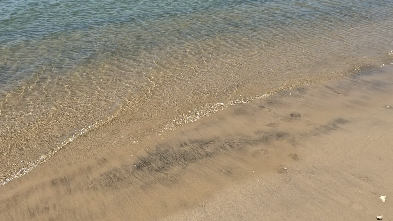 Clear shallow water laps across tan sand in Baja California, Mexico, with fine ripples and no visible people.