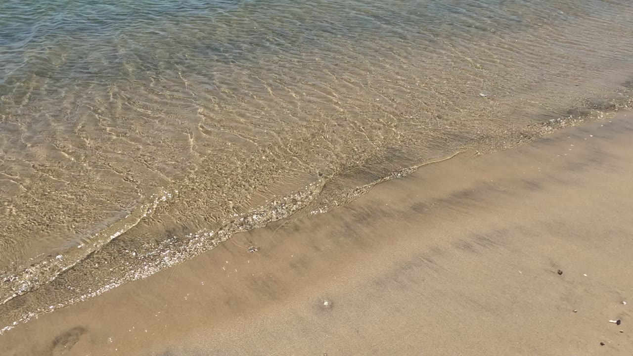 Rippled shallow water meets exposed sandy beach in Baja California, Mexico, with scattered shell pieces and no visible people.