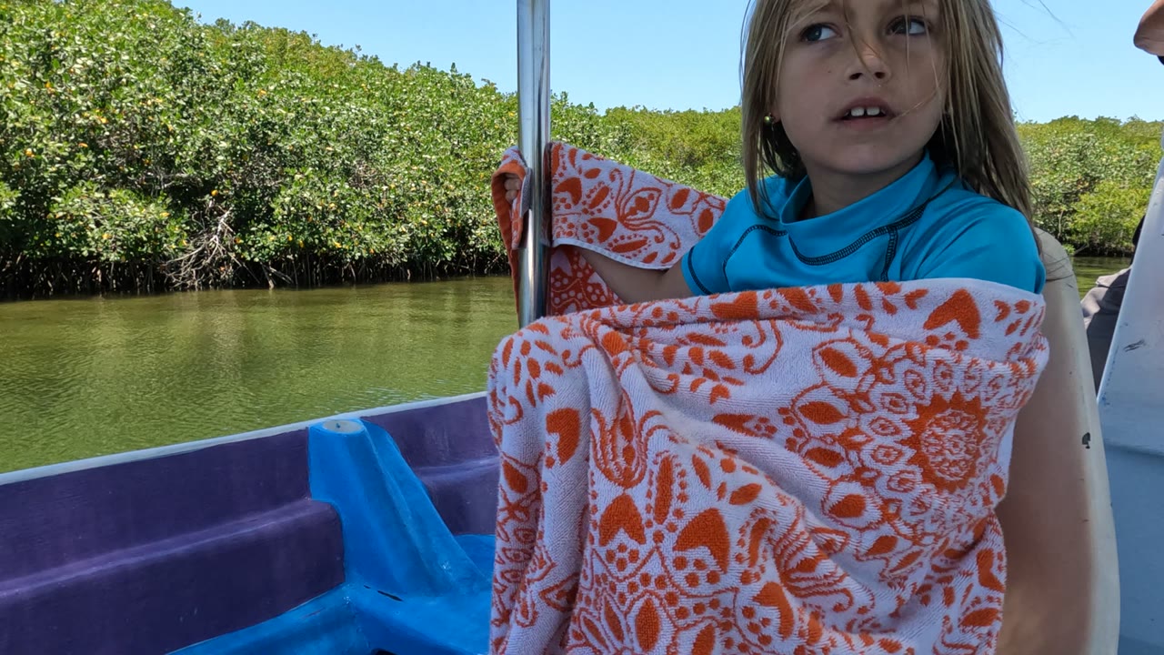Girl on a boat looks upward while wrapped in a patterned blanket.